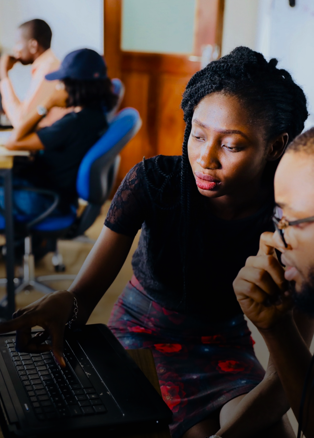 A young woman working on a computer with a male colleague in a classroom.